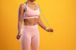 © Prostock-studio - A person wearing a pink workout outfit stands against a bright yellow backdrop, holding a jump rope and preparing for a home exercise session focused on fitness and health improvement.