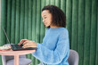 © Seventyfour - Side view of curly multiethnic young woman dressed in vibrant blue sweater typing on laptop working on project, while sitting in lounge area with designer furniture of modern coworking space