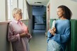 © Seventyfour - Side view of mature businesswoman casually chatting with younger employee of multiethnic background establishing intergenerational contact in workplace while standing in hallway, copy space