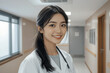© RooftopStudioBangkok - smiling female doctor in hospital corridor, wearing white coat and stethoscope, exuding professionalism and warmth