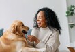 © Sandor - Smiling african american woman is playing with her golden retriever dog in the living room