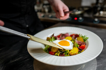 Wall Mural - A skilled chef plating a vibrant salad with roasted potatoes, cherry tomatoes, and a perfectly fried egg. The dish showcases fresh ingredients on a stylish white plate.