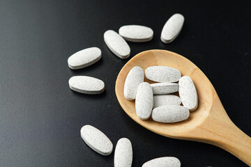 Wall Mural - white Pills Medicine tablet capsules in a wooden spoon blister pack on a black background