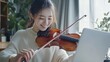 © Aliaksandr Siamko - a woman playing a violin while sitting in front of a laptop