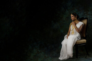 solo image of indian woman in a white saree wearing gold jewelry gold necklace gold bangles in a green solid background