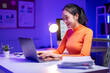 © Apichat - A woman is sitting at a desk with a laptop and a stack of papers
