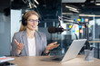 © Liubomir - Mature woman businesswoman in a modern office setting, using headphones and a microphone for podcast production. The image portrays professionalism and highlights a technological workspace.
