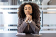 © Tetiana - Portrait of a young African American woman in a suit sitting in an office at a desk wearing a headset and with her hands folded together looking seriously at the camera