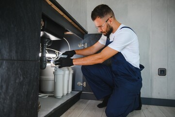 Plumber installs or change water filter. Replacement aqua filter. Repairman installing water filter cartridges in a kitchen. Installation of reverse osmosis water purification system