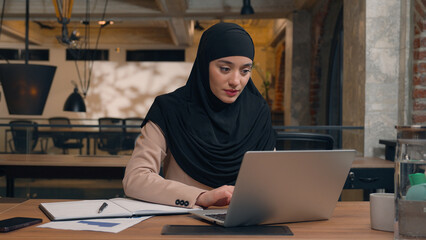 Wall Mural - Muslim woman in hijab female worker freelancer student Arabian businesswoman employee office manager agent online laptop remote work at workplace using computer pc smiling islamic girl business lady