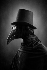 Wall Mural - Plague doctor with black vintage top hat at night over dark misty background 