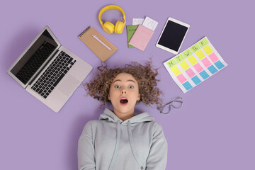 Canvas Print - Shocked young woman with modern gadgets, passports and business plan lying on lilac background, top view