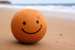 © wernerimages - A simple, orange ball adorned with a smiling face rests on a sandy beach by the sea, symbolizing carefree moments and childhood fun, under a clear sky.