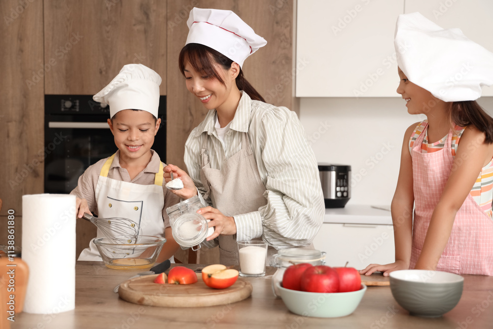 Female Asian chef with her little children making dough at table in kitchen