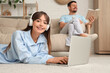 © Pixel-Shot - Young happy woman in pajamas with laptop and his boyfriend reading book at home