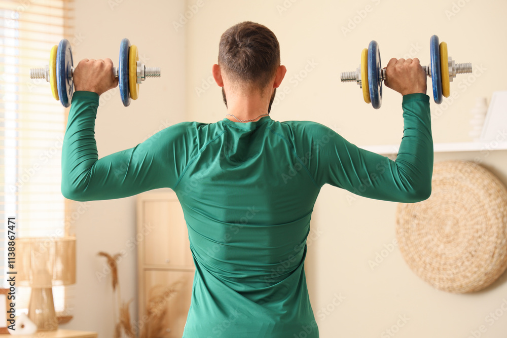 Sporty young man exercising with dumbbells at home, back view