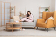 © Pixel-Shot - Young woman in striped pajamas working with laptop on sofa at home