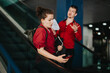 © qunica.com - Two business professionals in red shirts ascending an escalator in the city, engaged in conversation and using mobile devices.