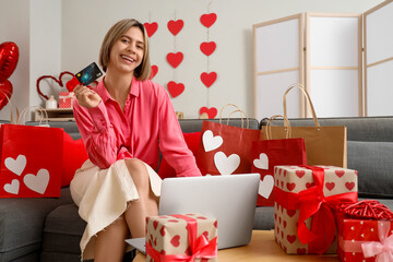 Wall Mural - Beautiful woman with credit card and laptop shopping online at home on Valentine's Day