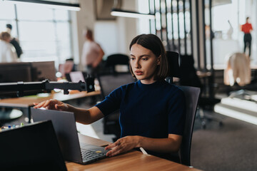 Wall Mural - A businesswoman concentrates on her laptop in a bright, modern office environment. This image captures the diversity and productivity of a multicultural workplace. Ideal for business and technology