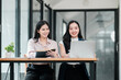 © Satori Studio - Two businesswomen working together in a bright, modern office, using a laptop and notebook for collaboration.