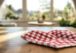 © adri - Red checkered cloth on wooden table, sunny kitchen background.