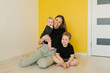 © Sunshine - Young mother and her two children are sitting on the floor in front of yellow wall. Conveys a warm atmosphere