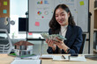 © Phimwilai - Asian sales girl, real estate agent holding money, counting money from house sale, customer's lease agreement, insurance while sitting at desk in office with model house in real estate project.