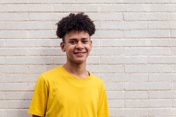 cheerful african american teenager male in casual clothes smiling happily standing against brick wall and looking at camera, concept of youth and urban lifestyle, copy space for text