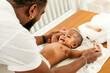 © artitwpd - A joyful father interacts with his smiling baby during a tender moment on a changing table, fostering connection and playfulness. Happy diversity family and newborn bathing concept.