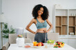 © Nuttapong punna - Smiling woman in a modern kitchen with fresh fruits, vegetables, blender, and orange juice, promoting clean eating, wellness