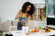 © Nuttapong punna - Smiling woman in a modern kitchen with fresh fruits, vegetables, blender, and orange juice, promoting clean eating, wellness