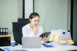 © laddawan - Asian female office worker business suits smiling at camera with working notepad, tablet and laptop documents