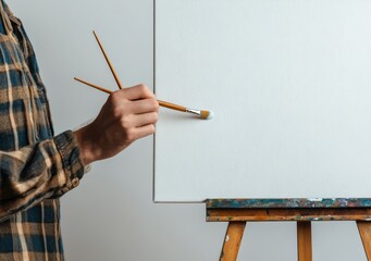 Aufkleber - A person holding a brush poised to paint on a blank canvas on an easel.
