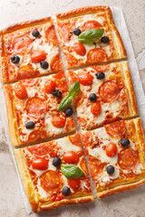 Wall Mural - Homemade puff pastry pie with sausage, olives, tomatoes and mozzarella cheese like pizza pepperoni close-up on parchment on table. Vertical top view from above