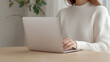 © AnuStudio - A person typing on a laptop while seated at a wooden table, wearing a cozy, knitted sweater, with greenery visible in the background.