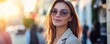 © HISTOCK - Businesswoman smiling wearing sunglasses in city street at sunset