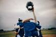 © Jacob Lund - Blue baseball team celebrating victory with players raising helmet in the air on a field