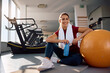 © Drazen - Happy sportswoman having water break while exercising in fitness center and looking at camera.