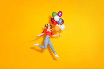 Wall Mural - Photo of young funky positive girl wearing blouse and jeans jump trampoline with gifts air balloons isolated on yellow color background