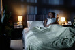 © AnnaStills - Mature African American man lying in comfortable bed and enjoying reading book at night in dark bedroom