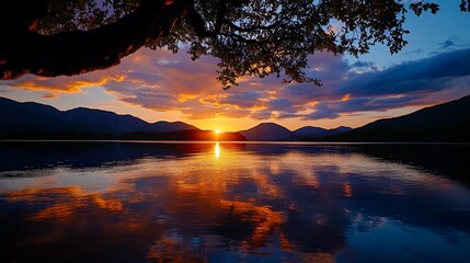 Wall Mural - Vibrant sunset reflecting on calm lake water, framed by tree branches and mountains.