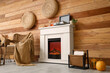 © Pixel-Shot - Interior of stylish room with wicker armchair, record player and autumn decorations on modern fireplace near brown wooden wall