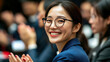 © ink drop - A happy smiling asian business woman at a conference meeting with people in the background