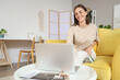 © Pixel-Shot - Young woman using laptop on yellow sofa at home