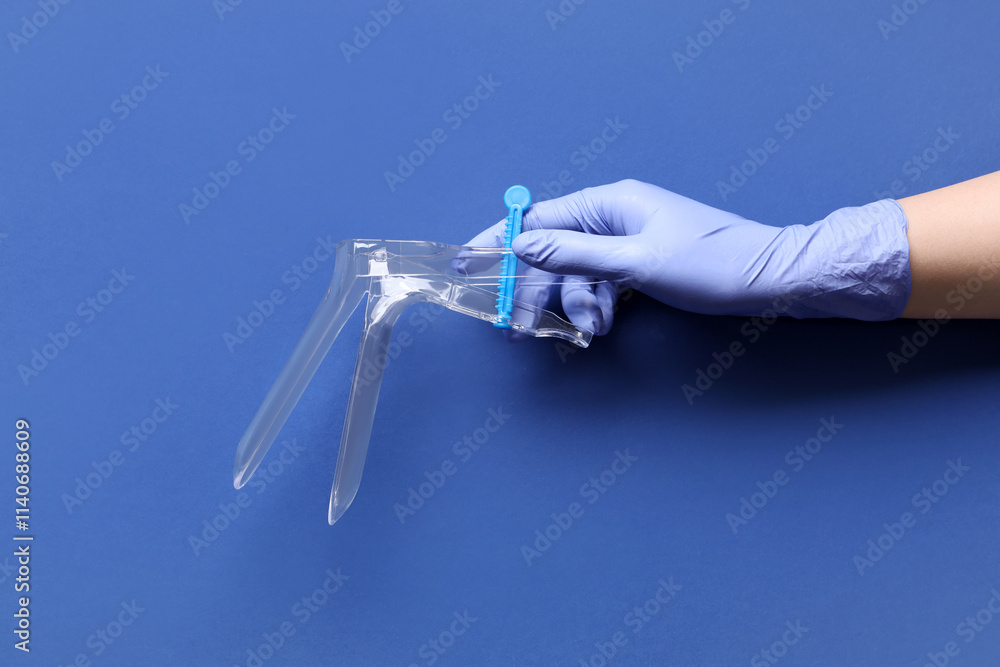 Doctor's hand with gynecological speculum on blue background