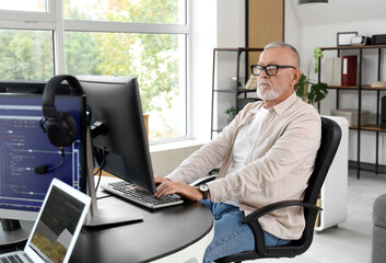 Wall Mural - mature programmer working with computer at table in office