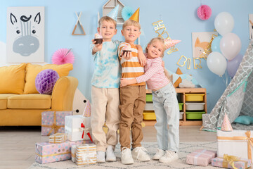 Wall Mural - Cute little happy kids in party hats with cupcakes and gift boxes celebrating birthday at home