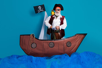 Photo of funny pirate in traditional costume swimming wooden boat isolated on blue color background