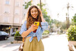 © maxbelchenko - Smiling young woman walking around old street using smartphone. Communication, social networks, online shopping concept.